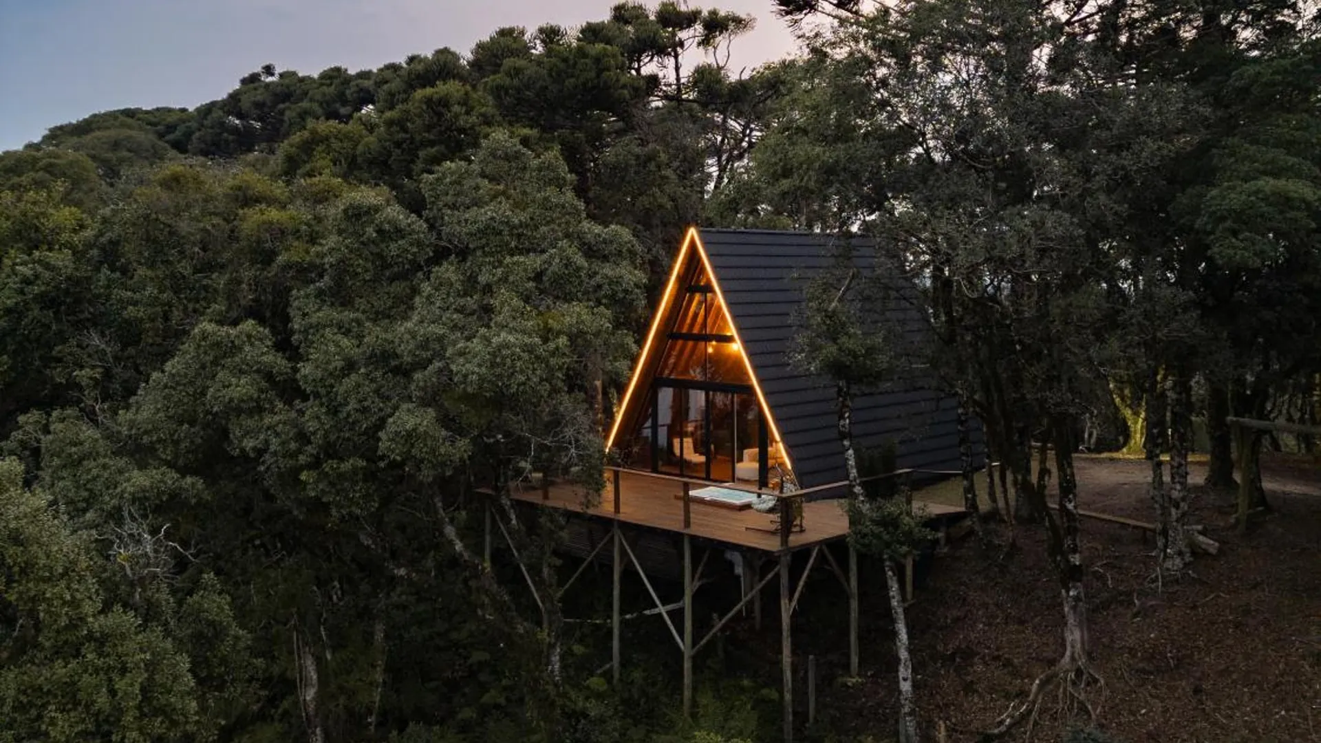 Cabana Araucária iluminada ao entardecer, sobre o deck suspenso no meio da mata de araucárias